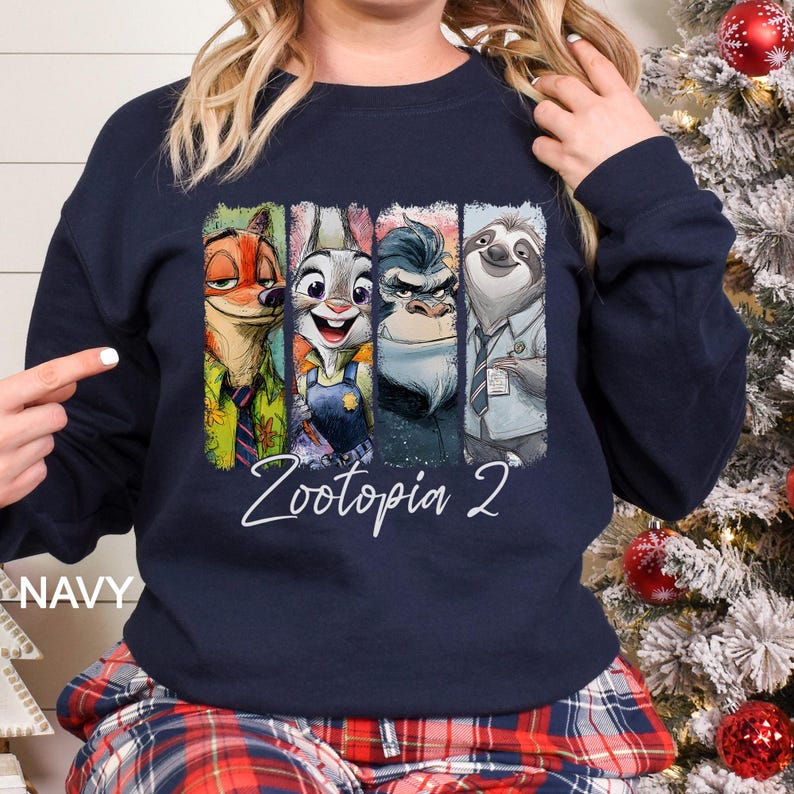 Puede incluir: Sudadera azul marino con un gr&aacute;fico colorido de los personajes de la pel&iacute;cula "Zootopia 2". El dise&ntilde;o incluye a Nick Wilde, Judy Hopps, el Jefe Bogo y Flash. Las palabras "Zootopia 2" est&aacute;n escritas en blanco debajo.