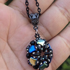 May include: A black beaded necklace with a silver pendant featuring a round, iridescent, multi-colored bead cluster.