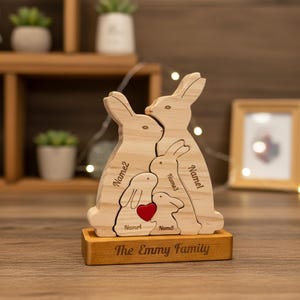 May include: A wooden family bunny figurine with five bunnies of varying sizes. The bunnies are light brown with engraved names and a red heart. The base is engraved with "The Emmy Family".