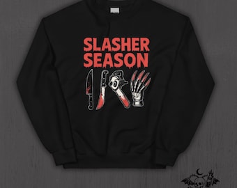 May include: Black sweatshirt with the text "SLASHER SEASON" in red. Below the text are illustrations of a bloody knife, chainsaw, and bladed glove. The Nocturnal Nursery Co. logo is in the bottom right corner.