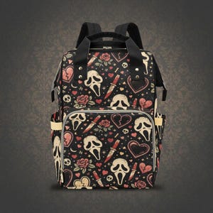 May include: Black backpack featuring a repeating pattern of Scream masks, hearts, roses, and knives. The bag has two side pockets, a front pocket, and a top handle. The bag has black straps and a black top handle.
