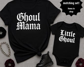 May include: Black t-shirts and a baby bodysuit with white gothic lettering that reads "Ghoul Mama" and "Little Ghoul." The image includes a black boot, scrunchies, and a silver chain. A matching set is advertised.