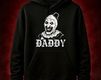 May include: Black hooded sweatshirt featuring a white graphic of a sinister clown face with a small hat and ruffled collar. The word "DADDY" is printed in a gothic font below the clown. The sweatshirt has a kangaroo pocket.