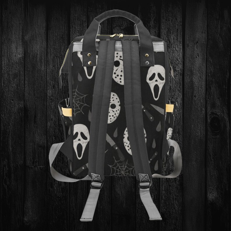 May include: Black backpack featuring a repeating pattern of white horror movie masks, knives, and spiderwebs. The backpack has a top handle, adjustable shoulder straps, and side pockets. The bag is made of a durable material.