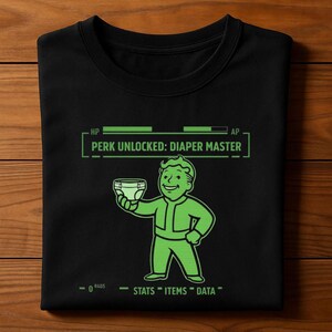 May include: Black t-shirt with a green graphic of a cartoon character holding a diaper, with the text "PERK UNLOCKED: DIAPER MASTER". The shirt also has the text "STATS", "ITEMS", and "DATA".