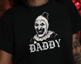 Könnte beinhalten: Ein schwarzes, kurzärmeliges bauchfreies Oberteil mit einem weißen Grafikdruck eines Clowns, der einen kleinen Zylinder und einen Rüschenkragen trägt. Unter dem Clown ist das Wort DADDY in einer verwaschenen, fetten weißen Serifenschrift gedruckt.