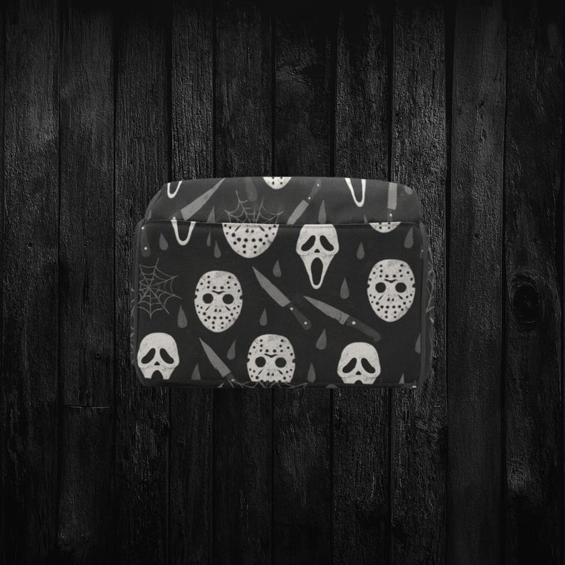 May include: Black accessory case featuring a repeating pattern of white horror movie masks, knives, and spiderwebs. The case has a rectangular shape and a black background. The design is a spooky, Halloween-themed pattern.