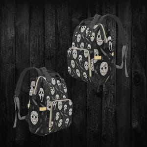 May include: Two black backpacks with a repeating pattern of white horror movie masks, knives, and spiderwebs. The backpacks have black straps, gold zippers, and a front pocket. The background is a dark wood.