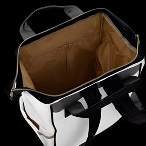 May include: Open black and white tote bag with a gold zipper and a tan interior. The bag has a geometric design and a handle. The interior has pockets. The bag is on a black background.