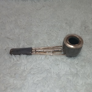 Peut inclure: Une pipe à fumer grise foncée avec un bord argenté et une tige grise foncée. La pipe a un cadre métallique et repose sur une surface blanche texturée.