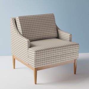 Puede incluir: Un sillón de tela a cuadros marrón y blanco con patas de madera. El sillón tiene un respaldo alto y un asiento ancho.