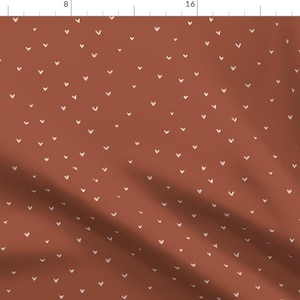 May include: A terracotta fabric with a repeating pattern of small white hearts.