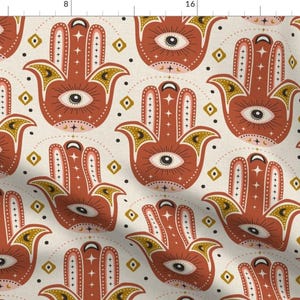 May include: A seamless pattern featuring a repeating design of red hamsa hands with a blue eye in the center. The hamsa hands are surrounded by gold and white geometric shapes on a cream background.