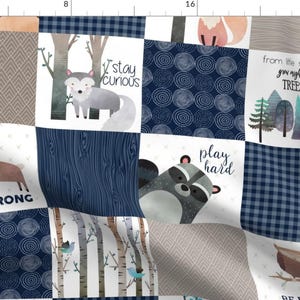 May include: A blue and white patchwork fabric with various woodland animal illustrations and inspirational quotes. The fabric features a moose, wolf, raccoon, owl, and trees. The quotes include "Be Strong", "Stay Curious", "Play Hard", "From the seeds grow mighty trees", and "Be Wise".