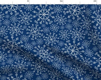 May include: A fabric with a repeating pattern of white snowflakes on a dark blue background. The snowflakes vary in size and have intricate, detailed designs. The fabric is likely suitable for winter-themed crafts or apparel.