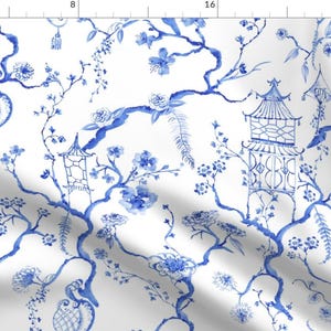 May include: White fabric with a blue watercolor Chinoiserie design. The pattern features pagodas, floral branches, and hanging lanterns. The design is a repeating pattern of blue and white.