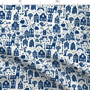 Peut inclure: Un tissu blanc avec un motif répétitif bleu et blanc de maisons, moulins à vent, arbres et fleurs. Le motif rappelle l'art populaire néerlandais.