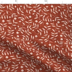 May include: A rust-colored fabric with a white floral pattern. The pattern features small white flowers and leaves.