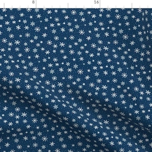May include: A navy blue fabric with a repeating pattern of white snowflakes and small white dots. The snowflakes vary in size and shape, creating a wintery or holiday theme. The fabric is likely used for apparel or home decor.