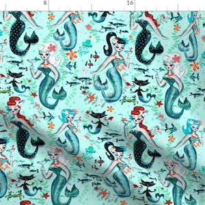 May include: A turquoise blue fabric with a repeating pattern of mermaids, black cats, and fish. The mermaids are wearing blue and green tails and have red, blonde, and black hair. They are holding cocktails. The black cats are wearing blue and green tails and have white eyes. The fish are blue and green.