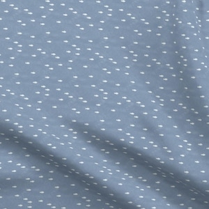 Pu&ograve; includere: Un tessuto blu chiaro con un motivo a pois bianchi. Il tessuto ha una leggera lucentezza e una texture morbida.
