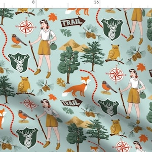 May include: Light blue fabric with a repeating pattern of outdoor adventure elements. The design includes illustrations of foxes, birds, trees, compasses, deer, and women hiking. The word "TRAIL" is also featured.