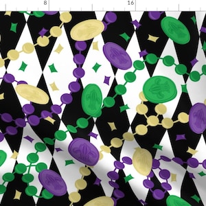 May include: A black and white diamond pattern fabric with purple, green, and gold beads and charms. The beads and charms are in the shape of fleur-de-lis.
