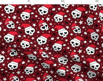 Puede incluir: Una tela roja con un patrón repetido de calaveras blancas que llevan gorros de Papá Noel con corazones por ojos. El fondo está lleno de estrellas blancas y negras y puntos blancos.
