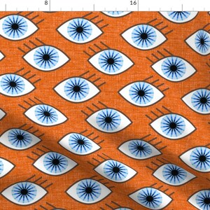 May include: Orange fabric with a repeating pattern of stylized blue eyes. Each eye has a white outline, a blue iris, and black eyelashes. The fabric has a textured appearance.