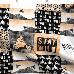 May include: A patchwork fabric design featuring a black and white motocross rider pattern, a black and white "Stay Wild" text, a black and white checkered flag pattern, and a black and white circle pattern. The background is a mix of orange and white.
