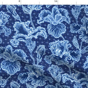 Puede incluir: Un patrón floral azul y blanco con un diseño repetitivo de flores de iris estilizadas. El fondo es azul oscuro con un patrón geométrico de estrellas blancas.
