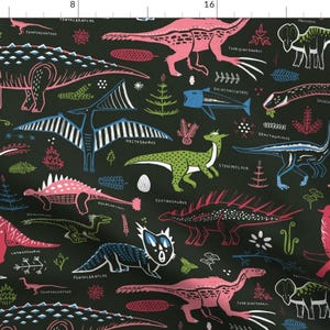 May include: A black fabric with a repeating pattern of colorful dinosaurs and prehistoric creatures. The dinosaurs are outlined in black and filled with pink, green, and blue colors. The fabric has a variety of different types of dinosaurs, including a stegosaurus, a pterodactyl, and a triceratops.