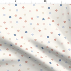 May include: Cream-colored fabric with a repeating pattern of randomly spaced polka dots in shades of dusty rose, light blue, and pale beige. The fabric is folded, creating shadows and depth.