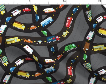 May include: A black and gray fabric with a repeating pattern of colorful vehicles driving on winding roads. The vehicles include a school bus, a fire truck, a fruit truck, a cement mixer, a delivery truck, and a police car. The roads are outlined in yellow.