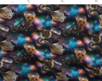 May include: A repeating pattern of cat faces against a dark blue background with swirling galaxies of pink, blue, and orange. The cats are in various poses, including looking directly at the viewer, looking away, and sleeping.
