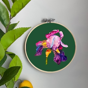 May include: A colourful embroidered iris flower on a green background in a wooden embroidery hoop.