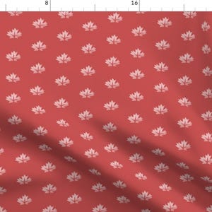 May include: A red fabric with a repeating pattern of white maple leaves.