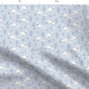 Pode incluir: Tecido azul claro com um padrão repetido de gansos brancos com laços azuis, acompanhados por seus gansinhos. O design também inclui elementos florais azuis, criando um tema caprichoso e pastoral. Ideal para decoração infantil ou projetos de artesanato.