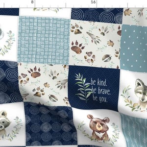 May include: A patchwork fabric design featuring woodland animals, including a badger, raccoon, wolf, and bear. The fabric is in shades of blue, white, and brown with a variety of patterns, including circles, dots, and paw prints. The text "be kind. be brave. be you." is printed on one of the squares.