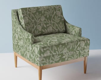 May include: A green armchair with a botanical pattern featuring light beige flowers and foliage. The chair has a wooden frame and legs. The upholstery covers the back, seat, and arms.
