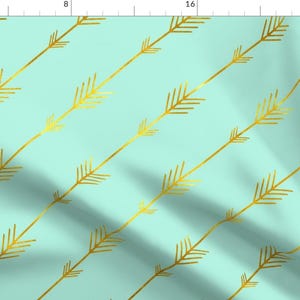 May include: A repeating pattern of gold arrows on a light teal background. The arrows are angled diagonally across the fabric. The design is simple and elegant, suitable for various craft projects.