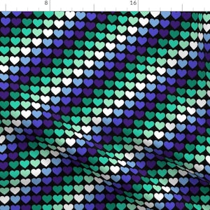 Puede incluir: Tela estampada con un patrón de corazones repetidos en blanco, turquesa, azul y morado sobre un fondo negro. Los corazones están dispuestos en filas y columnas, creando un efecto texturizado. Ideal para ropa o decoración del hogar.