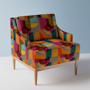 Puede incluir: Un sillón colorido con un patrón geométrico en tonos de rosa, naranja, amarillo, verde y gris. El sillón tiene un marco y patas de madera.