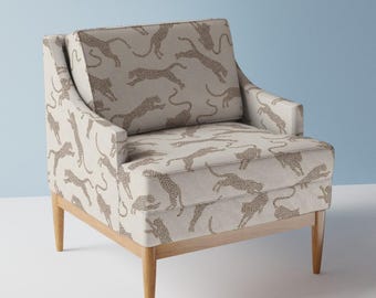 May include: A beige armchair with wooden legs features a repeating pattern of brown leopards on the fabric upholstery.