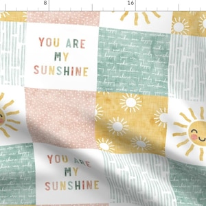 Puede incluir: Un diseño de tela de patchwork con un patrón repetitivo de soles y el texto "You are my sunshine" en colores arcoíris.