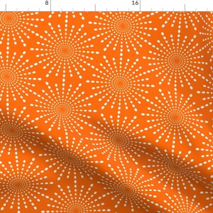 May include: A seamless pattern featuring white stylized sunbursts on a bright orange background. The sunbursts are made up of small white dots arranged in a circular pattern.