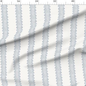 May include: A white fabric featuring a repeating vertical pattern of light blue lace-like stripes. The design consists of narrow, textured bands with scalloped edges, arranged in parallel lines across the surface of the textile material.