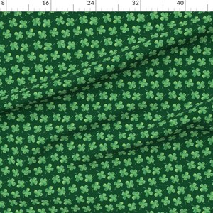 May include: A green fabric with a repeating pattern of four-leaf clovers. The clovers are a light green color and are scattered randomly across the fabric.