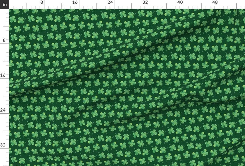 May include: A green fabric with a repeating pattern of four-leaf clovers. The clovers are a light green color and are scattered randomly across the fabric.