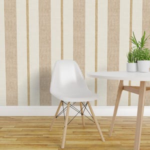 Può includere: Una sedia in plastica bianca stampata con gambe in legno chiaro e base in filo metallico nero, posizionata accanto a un tavolo rotondo bianco con una pianta verde in vaso, davanti a una parete con carta da parati a righe verticali beige e crema.